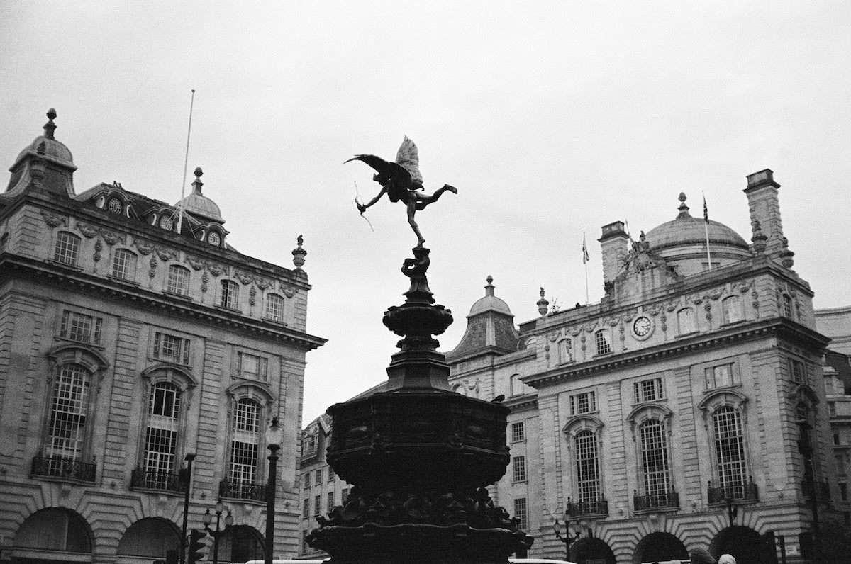 Black and white photo of a fountain with a statue in front of classical architecture