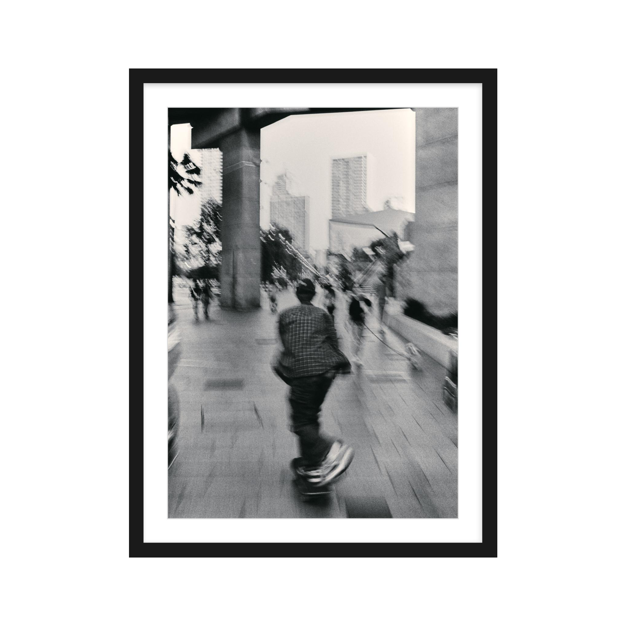 Framed black and white photograph of a person skateboarding on a city street.