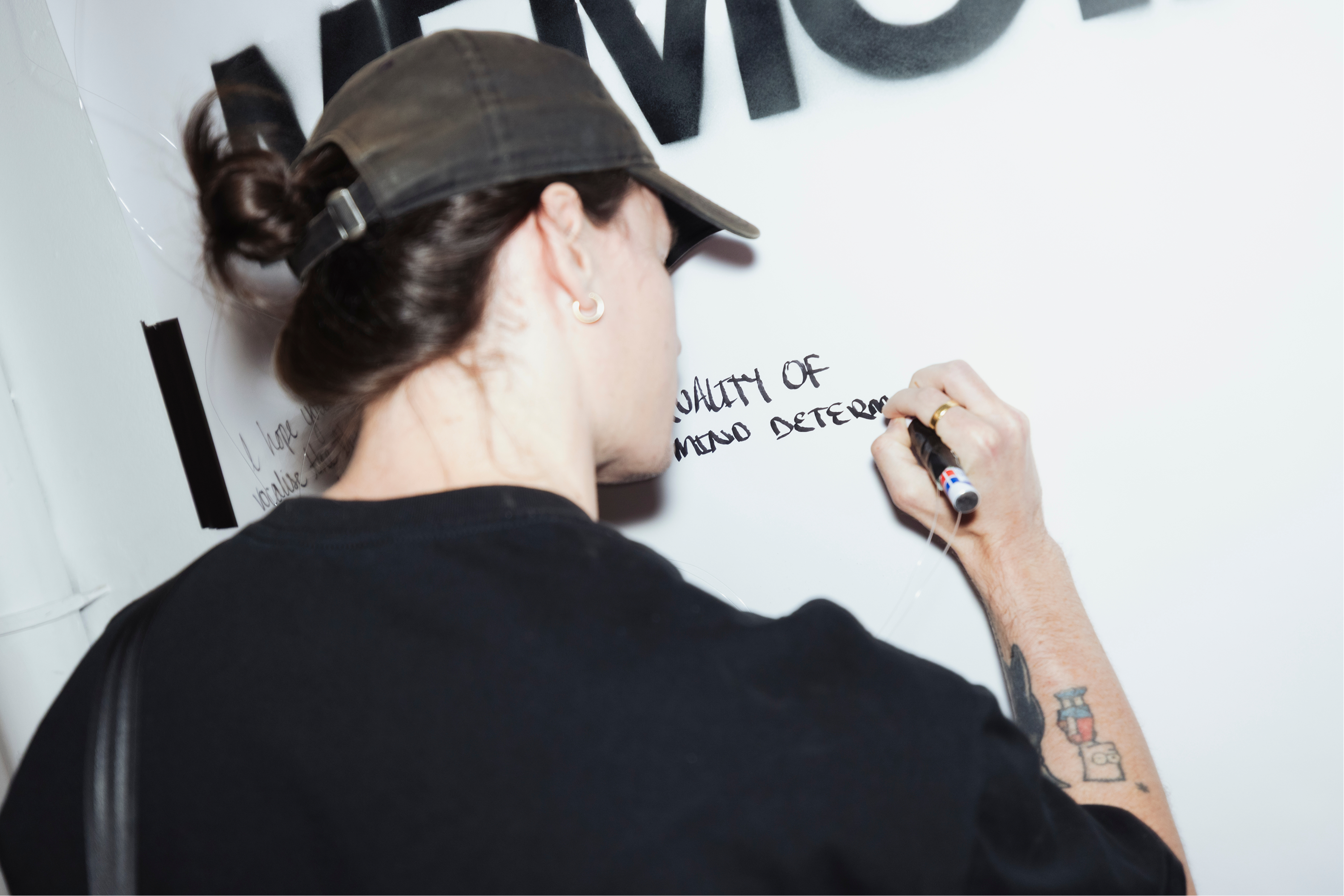 Person writing on a whiteboard for memoirs by him journal event with a marker, wearing a cap and black shirt.