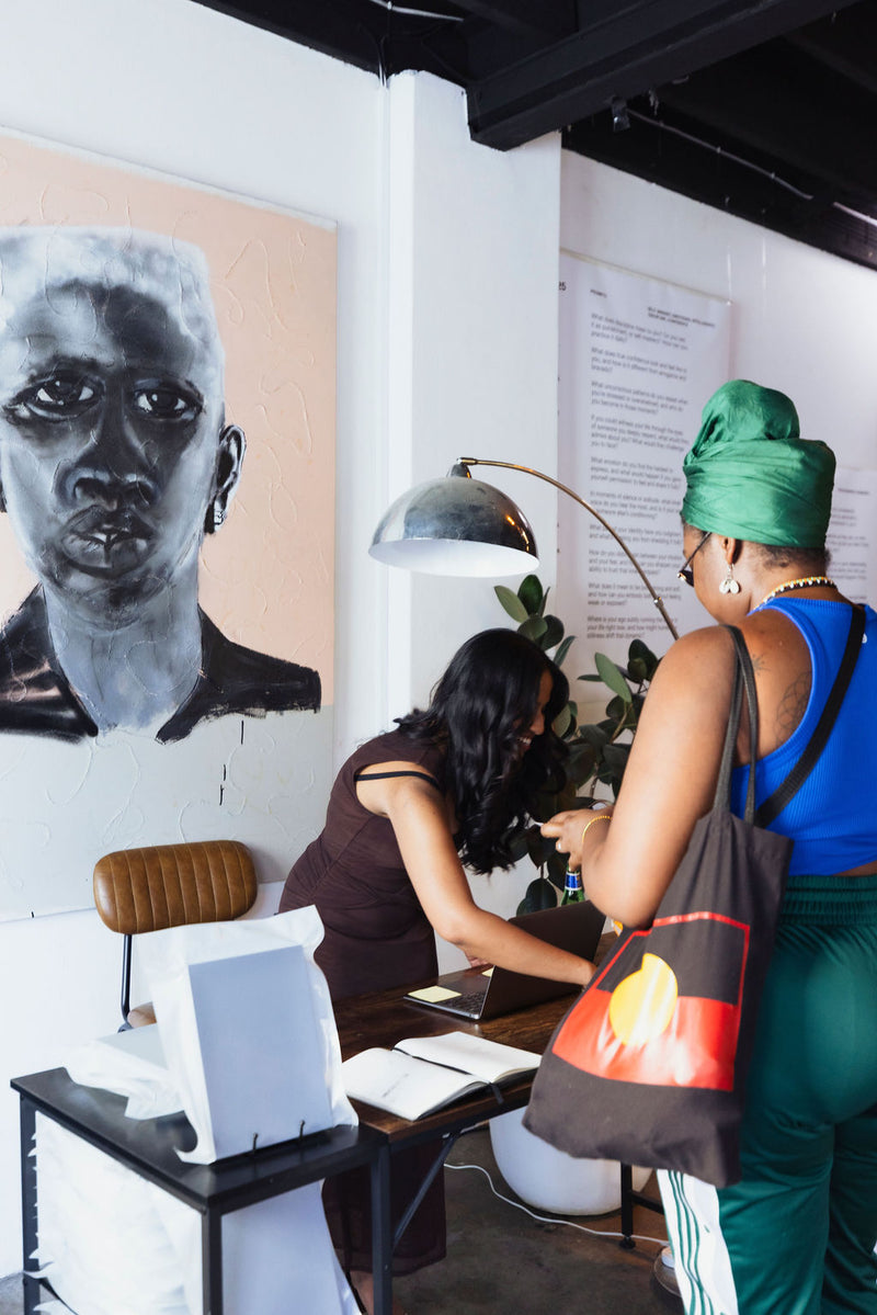 Two women in a room with a large portrait on the wall and a desk with a computer.