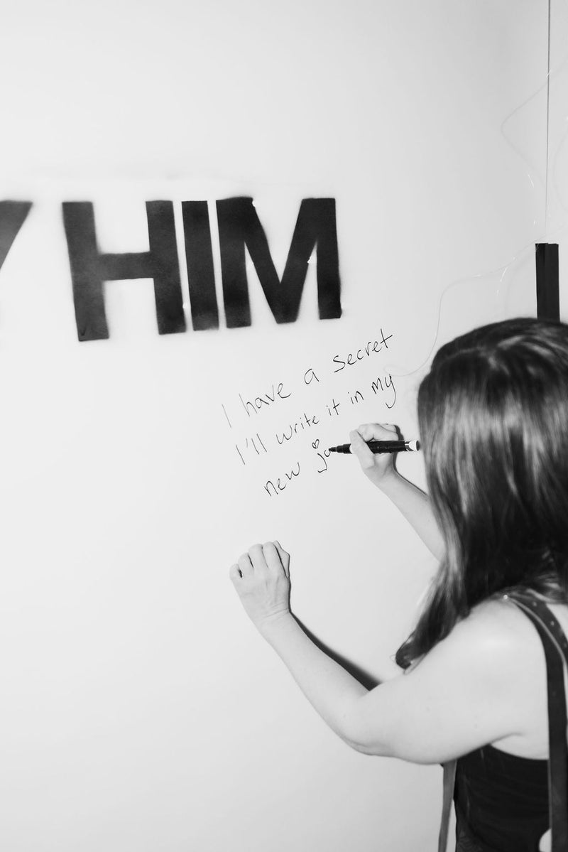 Person writing a journal entry on a wall with text, black and white photo