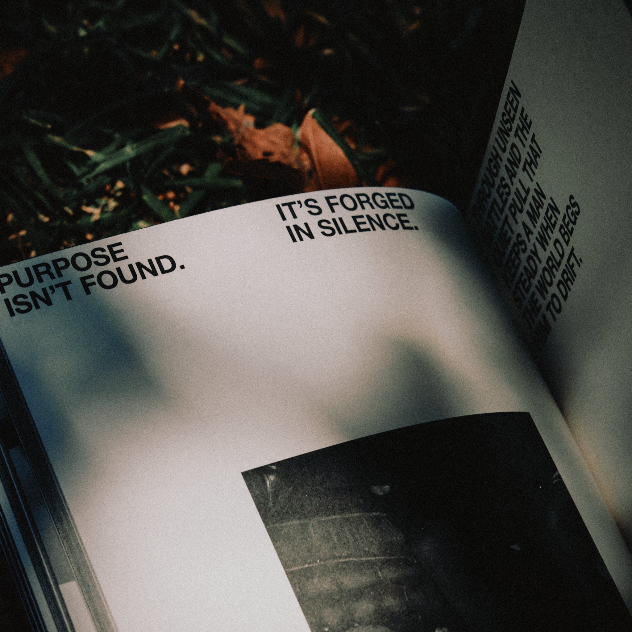 Open journal with text 'IT'S FORGED IN SILENCE. PURPOSE ISN'T FOUND.' on a blurred natural background
