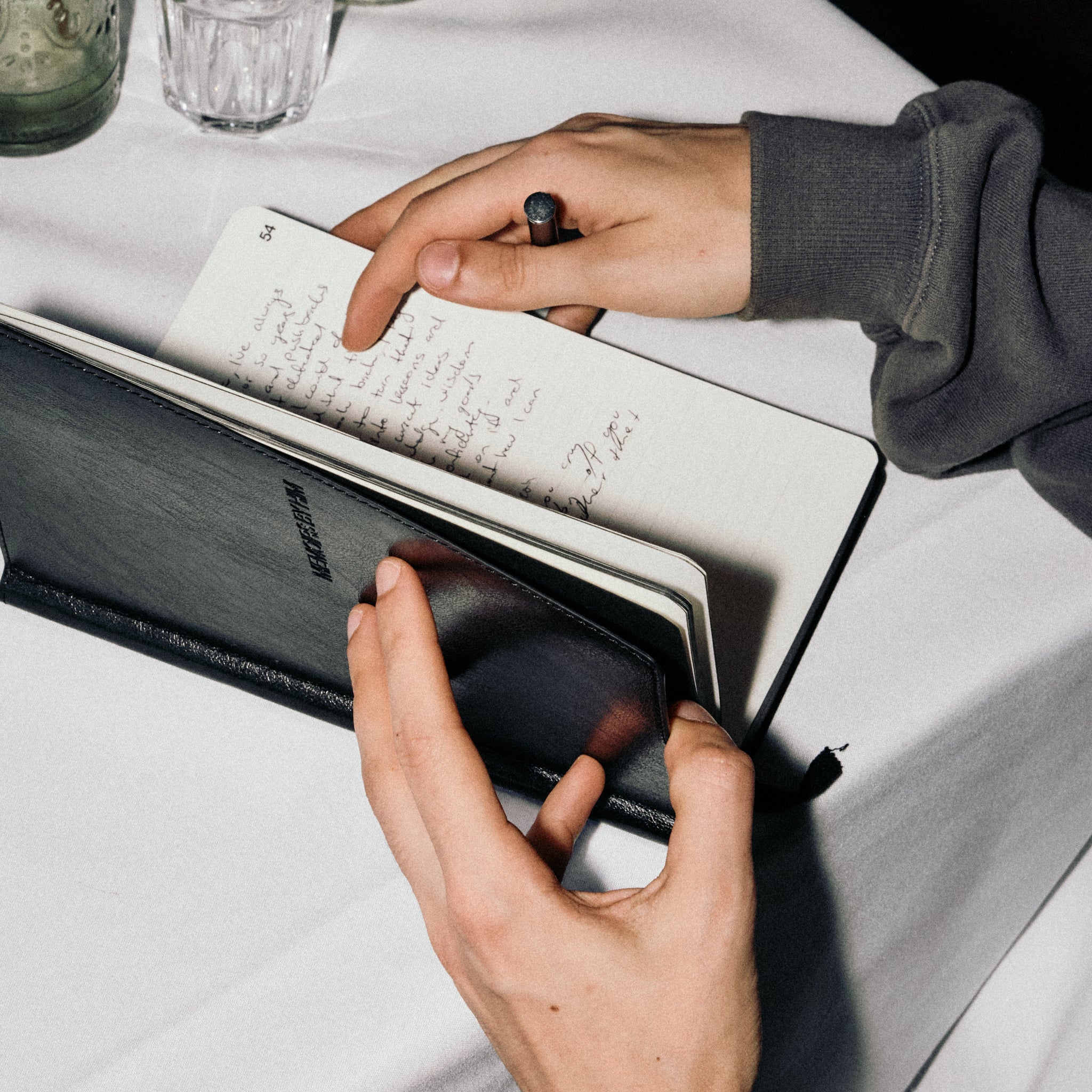Person writing in a journal with a pen on a light surface